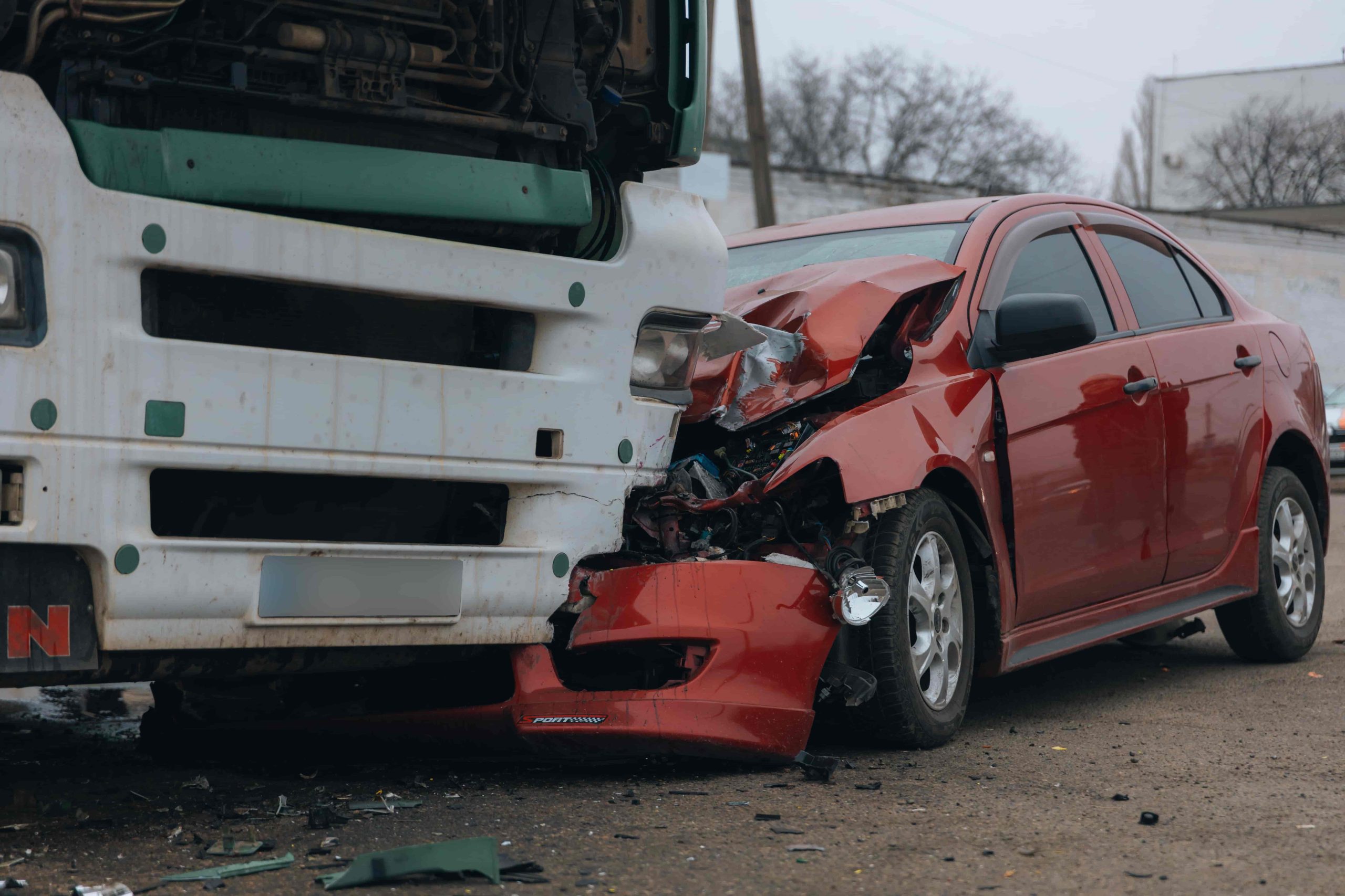Severe truck and car accident showing a red vehicle with front-end damage after collision with a large commercial truck.